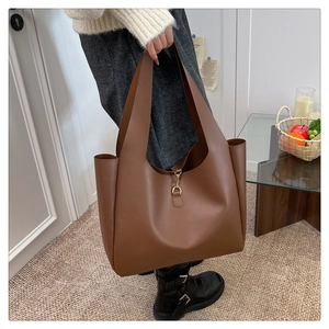 Detail of a brown matte leather tote bag featuring a decorative golden metal hook closure