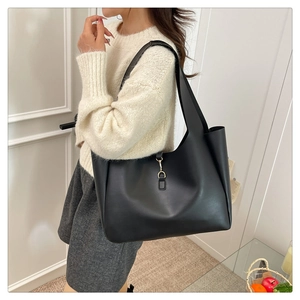 Detail of minimalist black leather tote bag featuring a golden buckle and wide shoulder strap