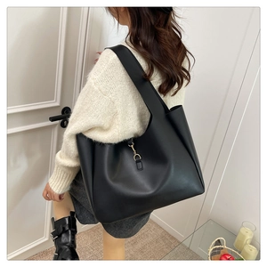 Large black matte leather tote bag styled on model in a minimalist home setting