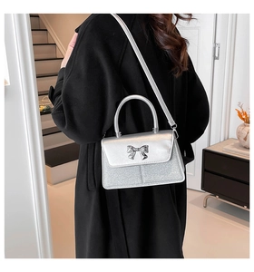 Detail view of silver crossbody bag featuring glitter texture and metal bow decoration