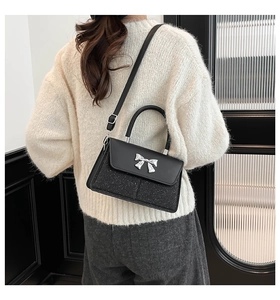 Detail of black crossbody bag with silver bow clasp and sequins on white fuzzy sweater
