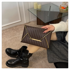 Détail de la texture tressée et du fermoir en métal doré sur la pochette marron foncé