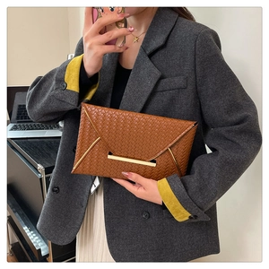 Braune geflochtene Umschlag-Handtasche mit goldener Schließe im modernen Outfit getragen