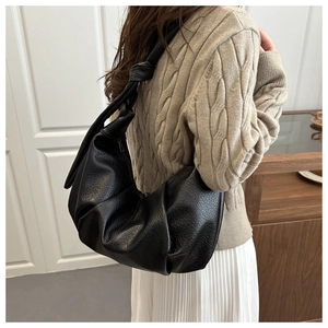 Détail des plis en cuir souple noir et bandoulière à nœud sur le sac rétro dumpling