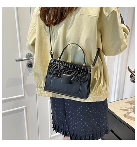 Detail of black crossbody bag with faux crocodile texture and elegant square buckle design