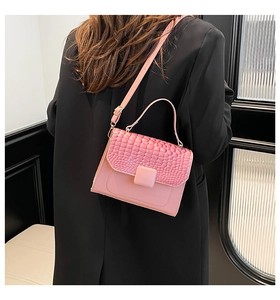 Sac à bandoulière rose avec rabat crocodile porté sur un blazer noir élégant