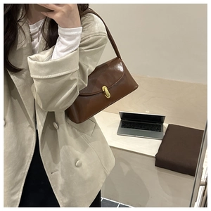 Close-up of a dark brown glossy leather underarm bag with a golden oval buckle lock