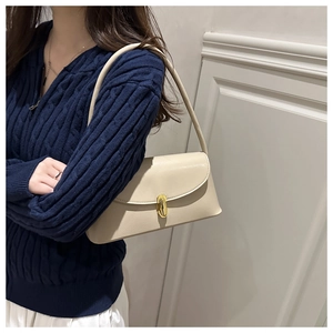 Chic cream white underarm bag with gold metal clasp on a stylish blue knit cardigan