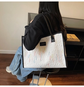 Detailed view of white quilted tote bag with rainbow embroidery and black shoulder straps