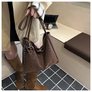 Detail of dark brown leopard jacquard tote bag with a cookie charm and striped scarf