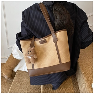 Detail of a large khaki tote bag featuring brown leather trim and a cute plush bear charm