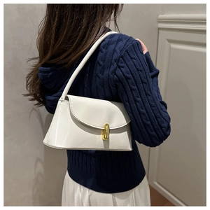 Close-up of a white glossy faux leather shoulder bag with a gold clasp and a navy sweater