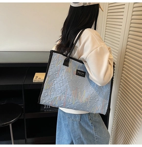 Detail of light blue quilted tote bag featuring vibrant wave embroidery and black handles