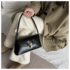 Detail of minimalist black leather underarm bag with cylindrical gold metallic buckle