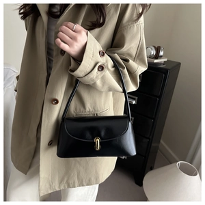Glossy black leather underarm bag with gold oval buckle shown on a model in a trench coat
