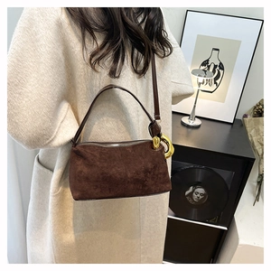 Gros plan du sac Boston en daim mat avec anneaux dorés et finitions métalliques chic