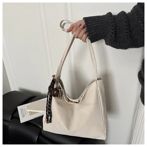 Detail of a large cream hobo tote bag featuring decorative silk ribbon and metal charms