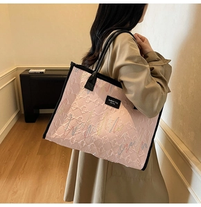 Pink quilted tote bag with wave embroidery and black handles shown on a wooden floor