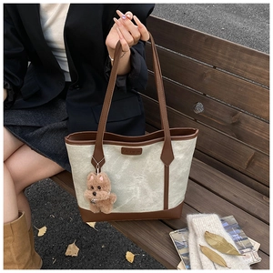 Detail of canvas tote bag with brown faux leather trim and plush puppy pendant accessory