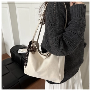 Detail view of a cream faux leather tote bag with a decorative silk scarf and metal ring