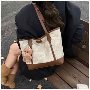 Dettaglio della borsa tote in tela con finiture in pelle marrone e ciondolo a orsetto