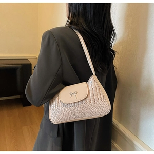 Detail of beige faux crocodile skin texture underarm bag with metal bow accessory