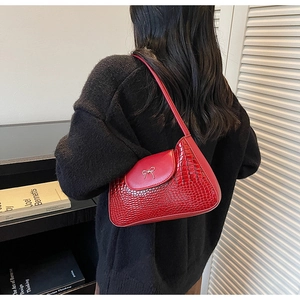 Detail of red crocodile texture underarm bag with silver metallic bow and smooth finish