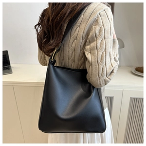 Detail of minimalist black leather crossbody bag with a prominent gold square buckle
