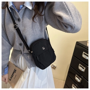 Detail of a black nylon crossbody bag with metal logo, shown on a female model