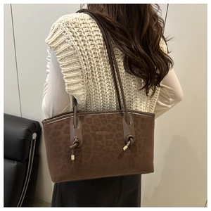 Detail of dark brown tote bag featuring leopard embossed texture and knotted shoulder strap