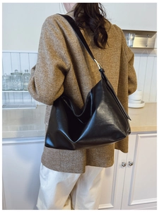Detail of a black large-capacity PU leather shoulder bag worn with a tweed blazer