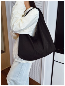 Detailed view of the large black nylon crescent tote bag worn by a model in casual style