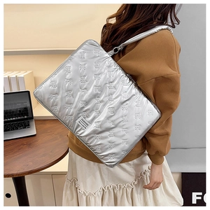 Silver quilted laptop bag with bow pattern and metal finish on a wooden desk