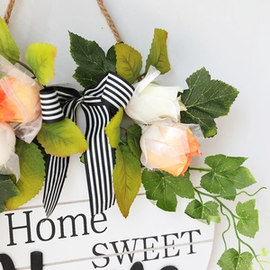 Detail of wooden welcome sign featuring artificial roses, green leaves and a striped bow