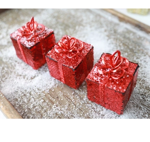 Drei rote Weihnachts-Geschenkboxen mit Pailletten und Schleifen auf verschneitem Holz