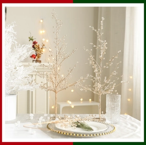 Détail de deux sapins de Noël dorés ornés de perles transparentes sur une table de fête