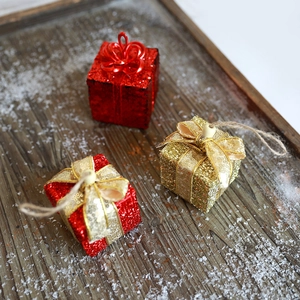 Drei glitzernde Weihnachtsgeschenkboxen in Rot und Gold auf einem verschneiten Tablett