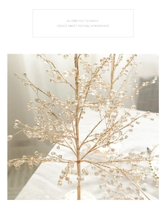 Détail d'une branche de Noël dorée ornée de perles sur une surface blanche