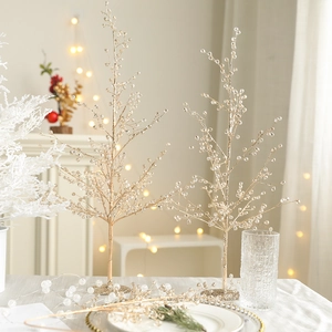 Lot de deux sapins de Noël dorés perlés sur une table décorée avec éclairage festif chaleureux