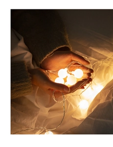 Close-up of warm white LED globe string lights held in hands for cozy room decoration