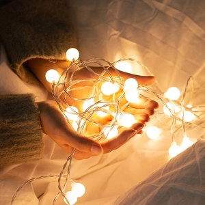 Warm white LED decorative ball light string held by hands for cozy home ambiance