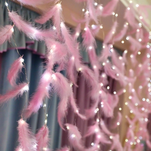 Détail d'une guirlande lumineuse LED à plumes roses avec lueur blanche sur fond textile