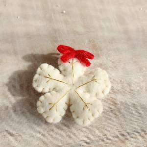 Detailed view of handmade white wool felt flower with red bow and gold embroidery