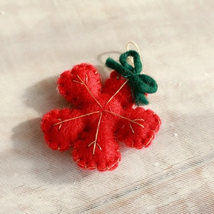 Macro detail of red wool felt snowflake ornament with gold embroidery and green bow