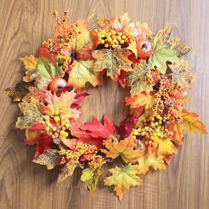 Detailed close-up of autumn wreath with maple leaves, berries and pumpkins on wood