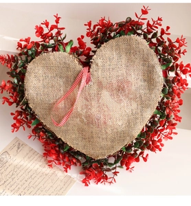 Macro shot of heart-shaped wreath with red leaves and a burlap center on white table