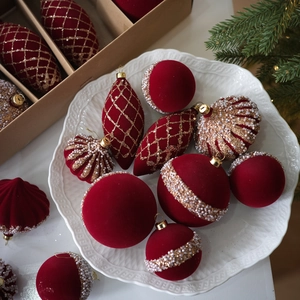Dark red flocked Christmas ornaments set with gold glitter and pearls in a white ceramic dish