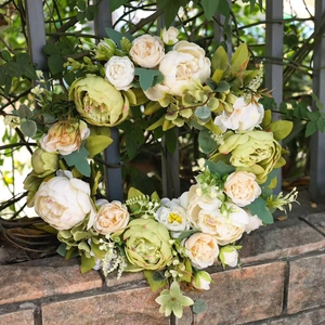 Couronne de porte avec pivoines crème et feuilles vertes sur une clôture métal