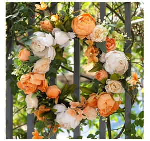 Detailansicht eines künstlichen Pfingstrosenkranzes mit orange-weißen Blüten am Zaun