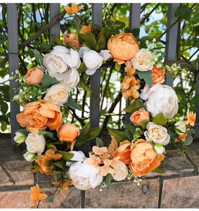 Detail eines künstlichen Pfingstrosenkranzes mit orangen Blüten an einem Metallzaun